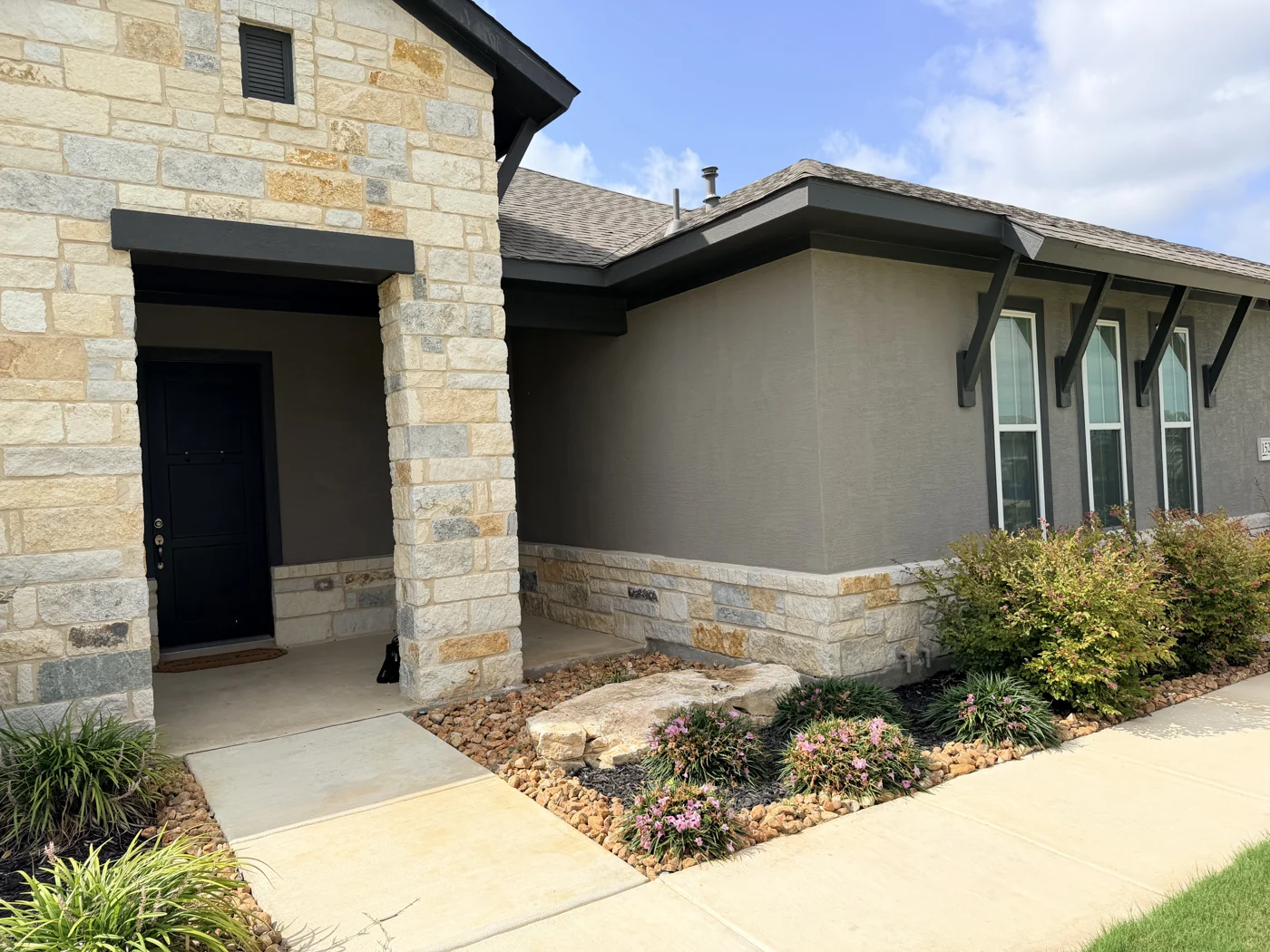 Stonework frames a dark entrance door beside the finished exterior walls.