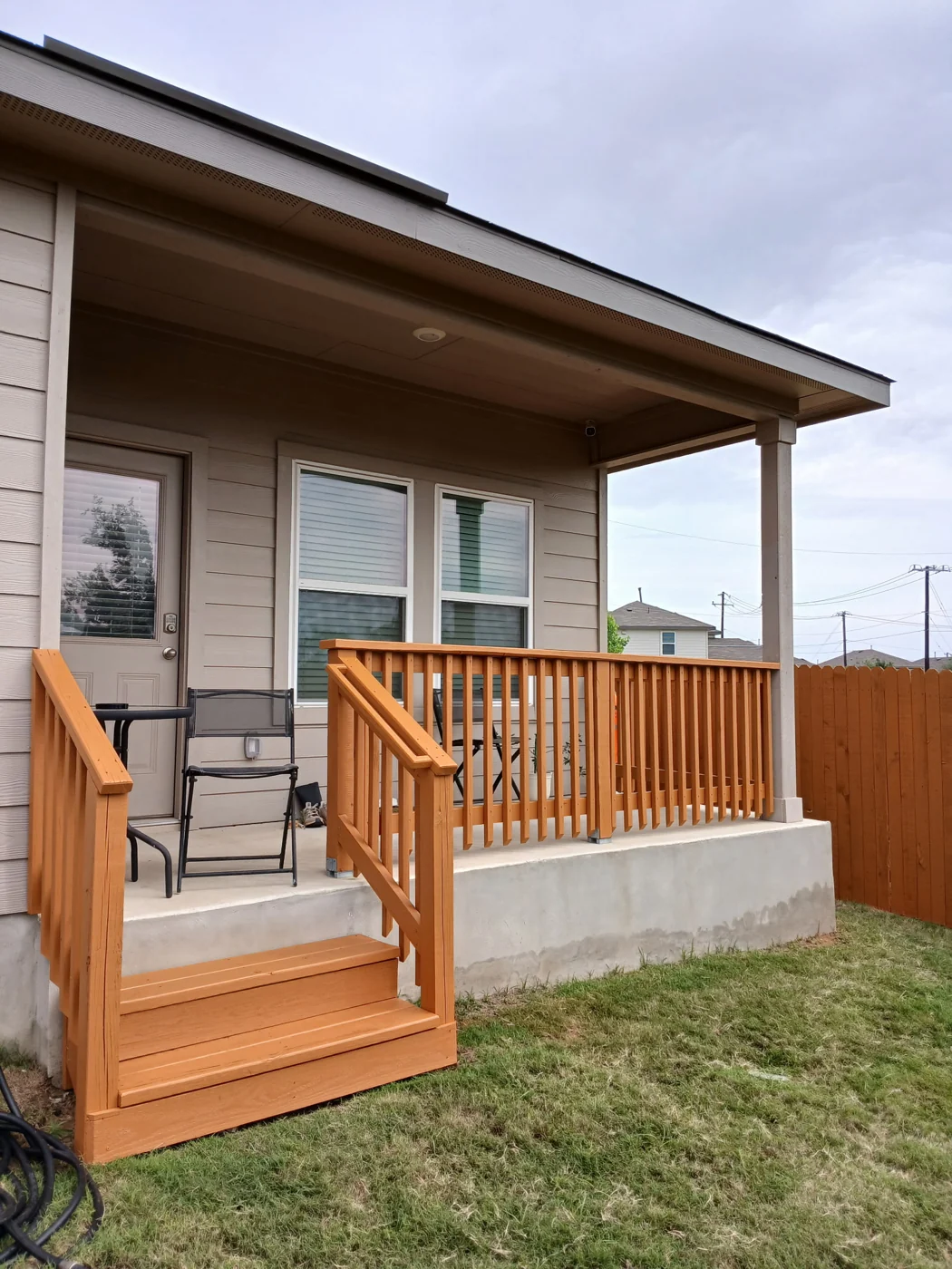 A wooden porch railing and steps beside the home and neighboring fence.