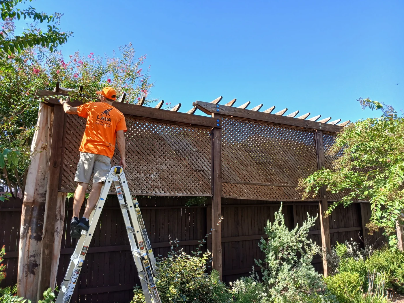 A crew member on a ladder working on an outdoor wooden structure.