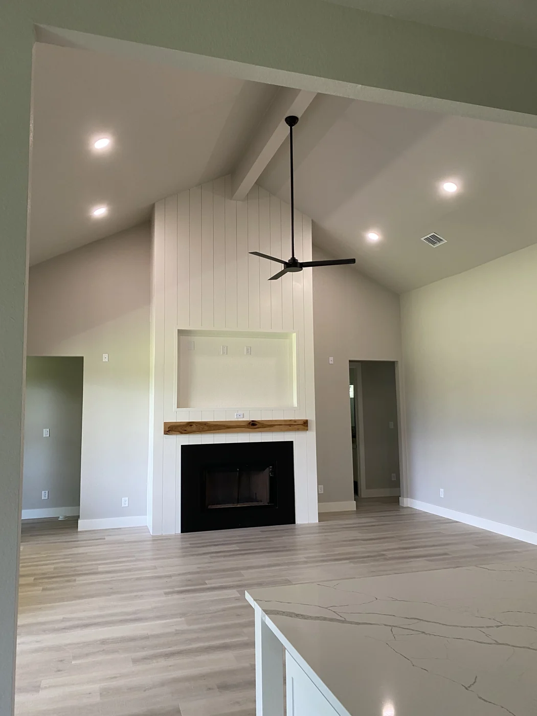 A finished living room with light walls, a tall fireplace surround and wood-look flooring.